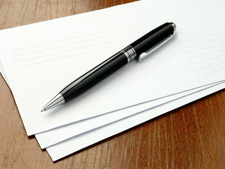 Schwarzer Kugelschreiber liegt auf einem Stapel weißer Blätter auf einer Holzoberfläche.